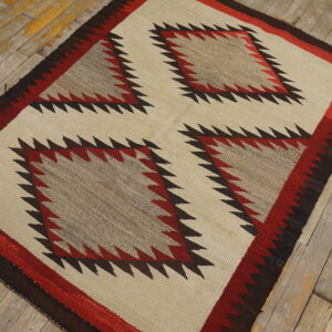 Cream and red geometric flatweave rug with serrated edges and four center diamonds on distressed wood planks.