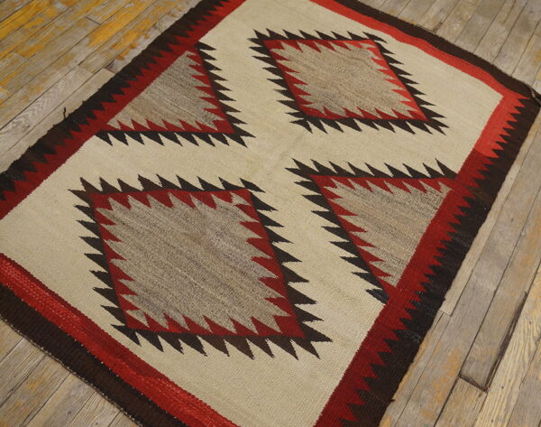 Cream and red geometric flatweave rug with serrated edges and four center diamonds on distressed wood planks.