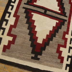 Geometric rug with stepped patterns in off-white, dark red, gray, and black on distressed yellow wood flooring.