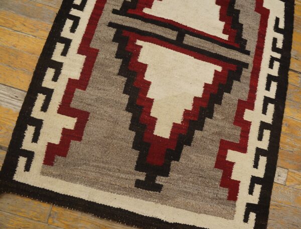Geometric rug with stepped patterns in off-white, dark red, gray, and black on distressed yellow wood flooring.