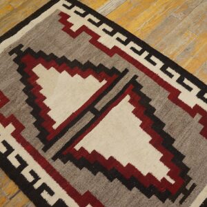 Low-pile rug with a red, gray, cream, and black geometric pattern on distressed wood floor.