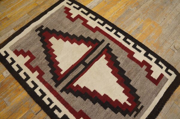 Low-pile rug with a red, gray, cream, and black geometric pattern on distressed wood floor.