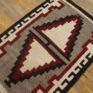 Low-pile rug with geometric patterns in cream, maroon, gray, and black on rustic wood floors.