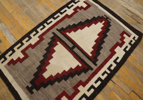 Low-pile rug with geometric patterns in cream, maroon, gray, and black on rustic wood floors.