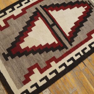 Geometric flatweave rug featuring stepped patterns in cream, red, gray, and black on distressed wood flooring.
