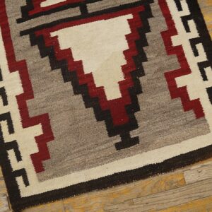 Cream, gray, red, and black flatweave rug with a stepped geometric pattern on worn wooden flooring.