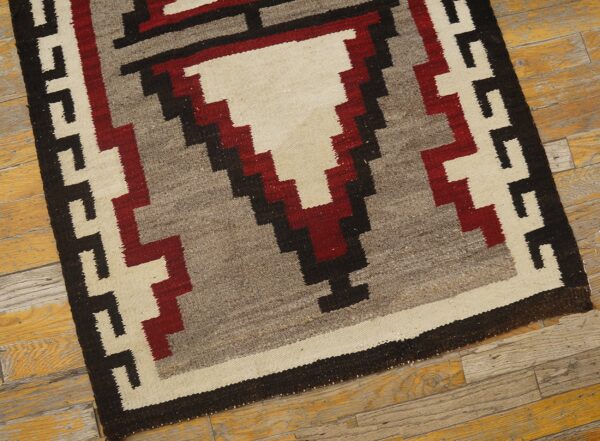 Cream, gray, red, and black flatweave rug with a stepped geometric pattern on worn wooden flooring.