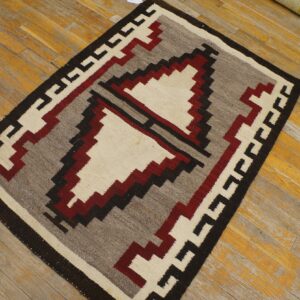 Flatwoven rug with cream, red, gray, and black geometric patterns resting on worn wood flooring.