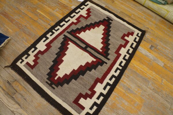 Flatwoven rug with cream, red, gray, and black geometric patterns resting on worn wood flooring.