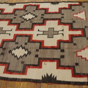 Beige, gray, black, and red geometric low-pile rug lying on a natural wood floor.