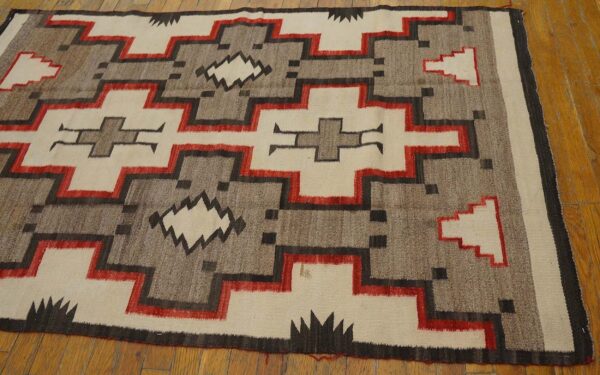 Beige, gray, black, and red geometric low-pile rug lying on a natural wood floor.