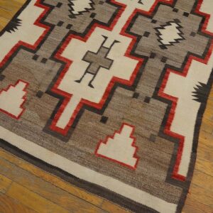 Low-pile rug with intricate cream, brown, black, and red geometric designs on wood planks.