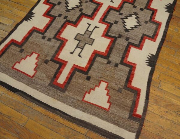 Low-pile rug with intricate cream, brown, black, and red geometric designs on wood planks.