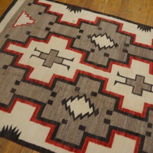 A flat-woven rug features stepped geometric patterns in cream, gray, red, and black on a wooden floor.