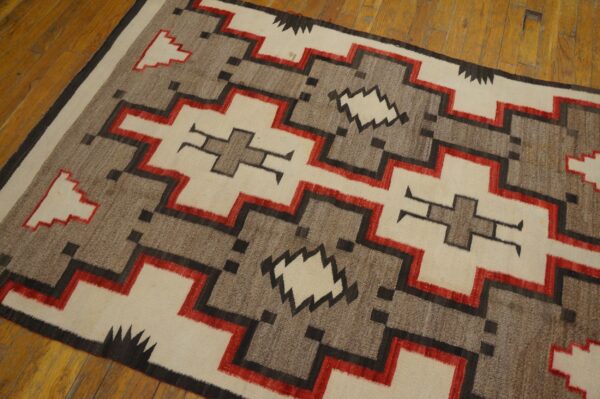 A flat-woven rug features stepped geometric patterns in cream, gray, red, and black on a wooden floor.