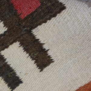 Woven rug detail showing stepped patterns in cream, red, and dark brown on weathered wood.