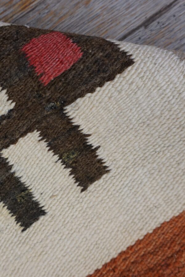 Woven rug detail showing stepped patterns in cream, red, and dark brown on weathered wood.