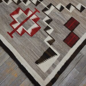 Gray flatweave rug with zigzag and diamond patterns in red, white, and dark brown on weathered wood.