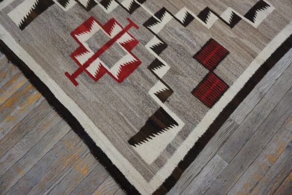 Gray flatweave rug with zigzag and diamond patterns in red, white, and dark brown on weathered wood.