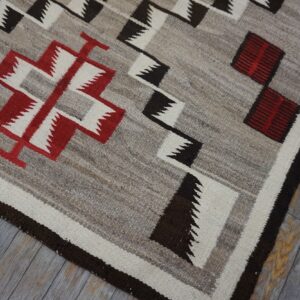 Gray flat weave rug with red, black, and white geometric patterns on wood planks.