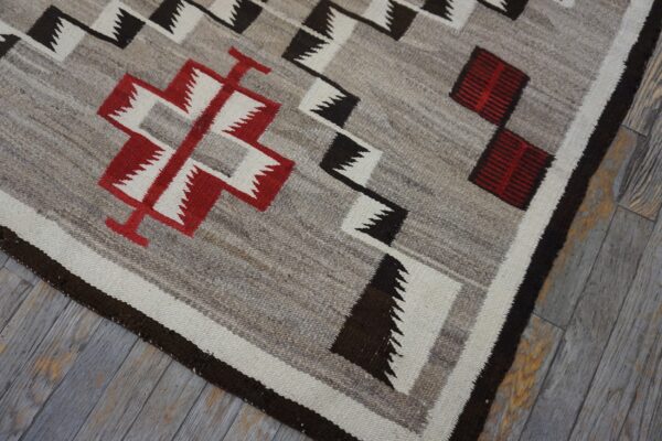 Gray flat weave rug with red, black, and white geometric patterns on wood planks.