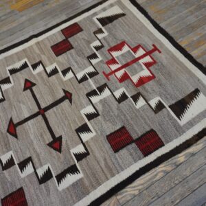 Low-pile geometric rug in gray, white, red, and dark brown on weathered wood floorboards.