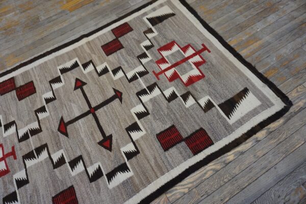 Low-pile geometric rug in gray, white, red, and dark brown on weathered wood floorboards.