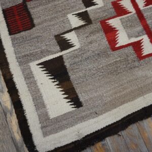 Low-pile rug with zigzag red, cream, and brown geometric patterns rests on distressed gray wood planks.