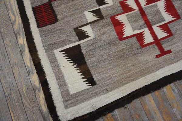 Low-pile rug with zigzag red, cream, and brown geometric patterns rests on distressed gray wood planks.