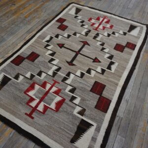 Natural gray rug featuring red, white, and dark geometric patterns rests on heavily weathered wood floors.