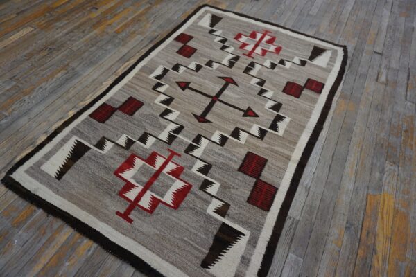 Natural gray rug featuring red, white, and dark geometric patterns rests on heavily weathered wood floors.