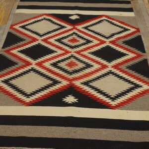 Black, red, and beige flat-weave rug with serrated diamonds lies on weathered wooden plank flooring.