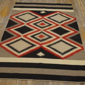 Red, black, and cream flatwoven rug with stacked geometric diamond designs on a worn plank wood floor.