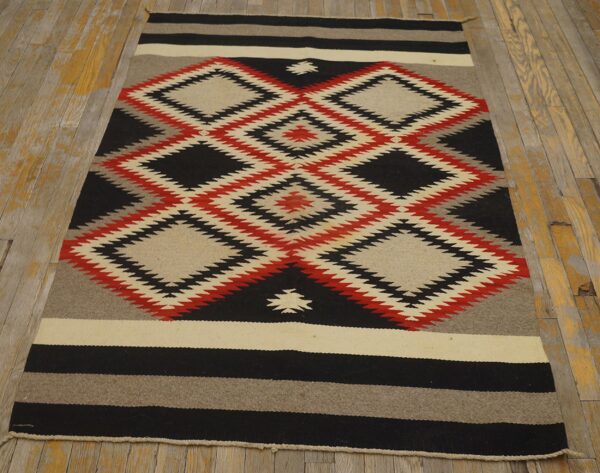 Red, black, and cream flatwoven rug with stacked geometric diamond designs on a worn plank wood floor.
