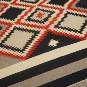 Flatweave rug featuring serrated diamonds in black, red, and cream, transitioning to wide striped bands.