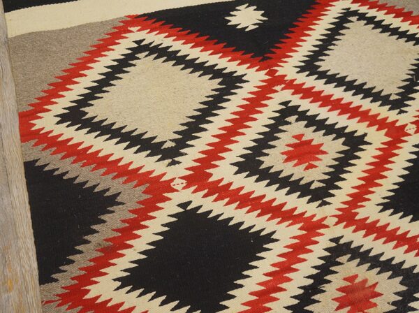 Flatweave rug with zigzag geometric patterns in black, red, cream, and gray on wood flooring.