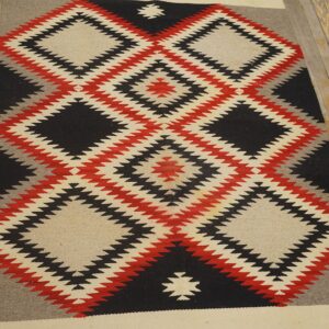 Flatweave rug in black, red, gray, and cream geometric diamond patterns rests on wood flooring.
