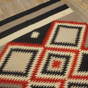 Black, red, and cream geometric rug with jagged diamonds rests on distressed light wood flooring.