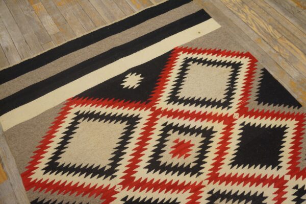 Black, red, and cream geometric rug with jagged diamonds rests on distressed light wood flooring.