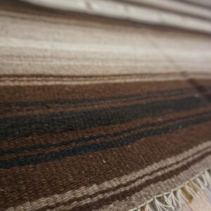 Close-up of a striped flatweave rug in natural browns and cream, resting on rustic wooden plank flooring.