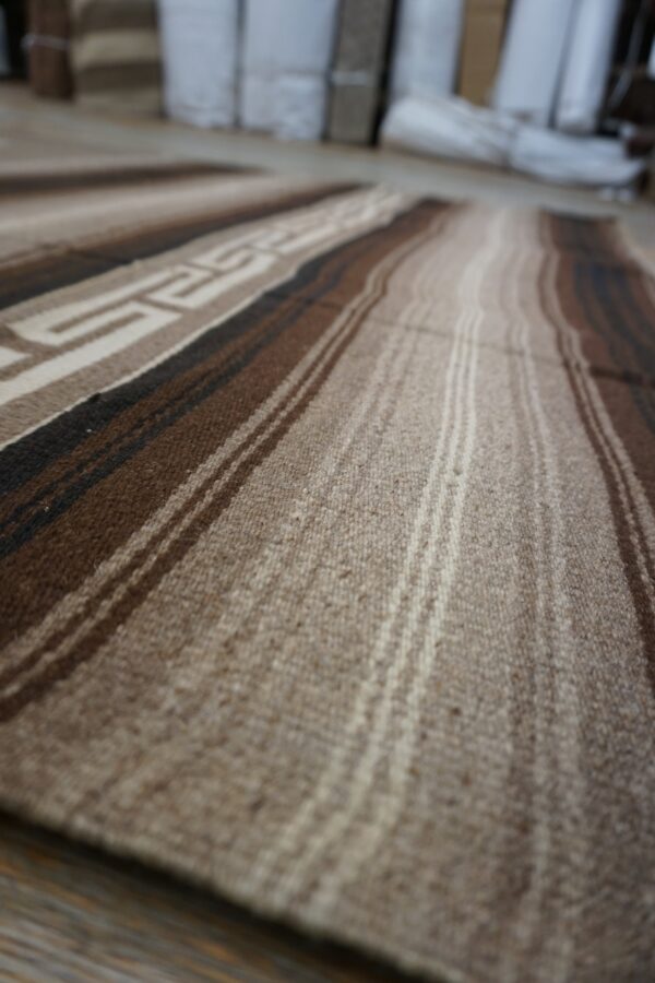 Striped rug in shades of natural brown and tan showing a woven geometric pattern detail.