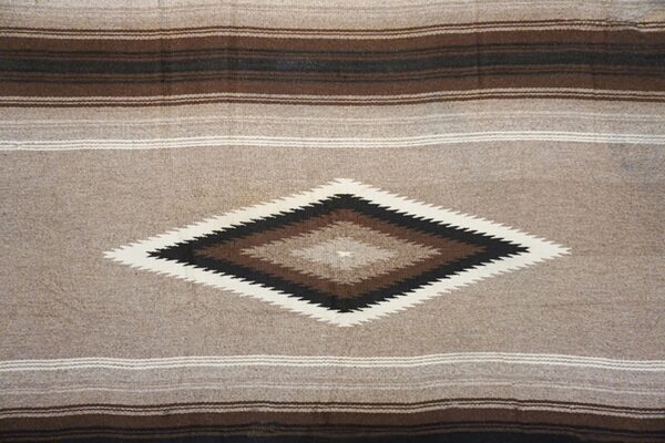 Low-texture rug in tan, brown, and black with horizontal stripes and a central serrated diamond pattern.