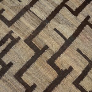 Textured, flatweave rug featuring a dark brown geometric key pattern on a neutral tan patchwork ground.