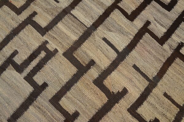 Textured, flatweave rug featuring a dark brown geometric key pattern on a neutral tan patchwork ground.