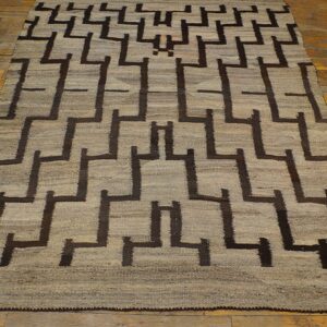 A low-pile rug in light tan and dark brown with a repeating geometric maze design on hardwood floors.