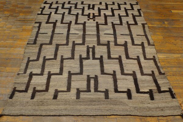 A low-pile rug in light tan and dark brown with a repeating geometric maze design on hardwood floors.