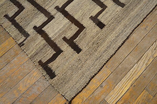 Beige and dark brown geometric flatweave rug covering a section of distressed natural wood plank flooring.