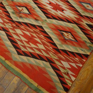 Geometric flatweave rug in red, black, cream, and green lays over wide, amber-toned wood planks.