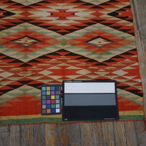 Flat-woven rug with orange, black, and green geometric patterns covers weathered wooden floorboards.