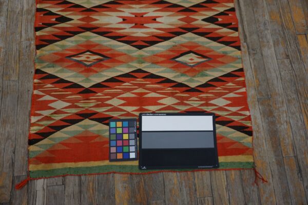 Flat-woven rug with orange, black, and green geometric patterns covers weathered wooden floorboards.